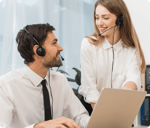 A man and woman, both equipped with headsets, are intently working together on a laptop in a collaborative environment.