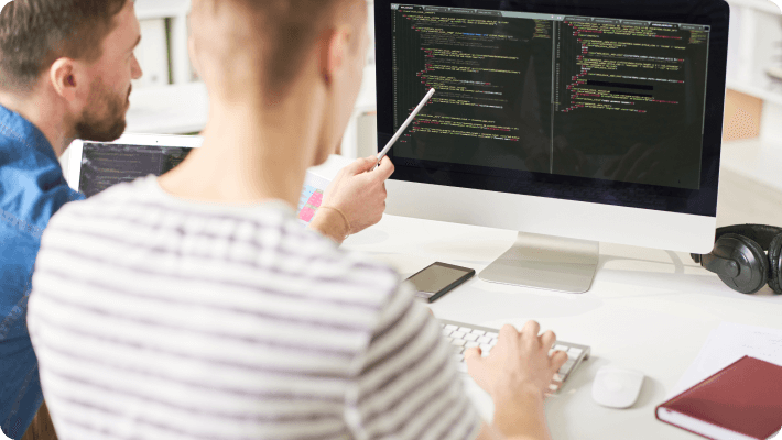 Two men engage in programming work together, analyzing code on a computer screen.