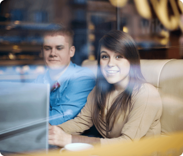 A man and woman at a table, focused on a laptop, indicating a collaborative work or discussion environment.
