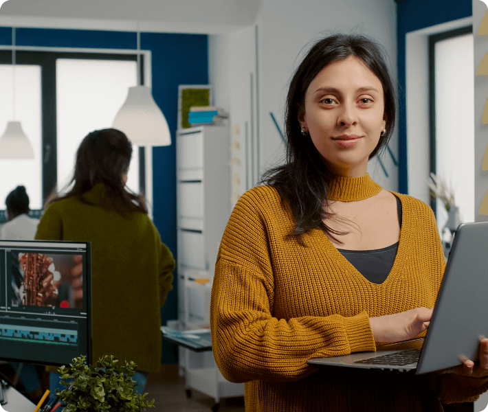 In an office, a woman confidently holds a laptop, engaged in her tasks with a determined expression.
