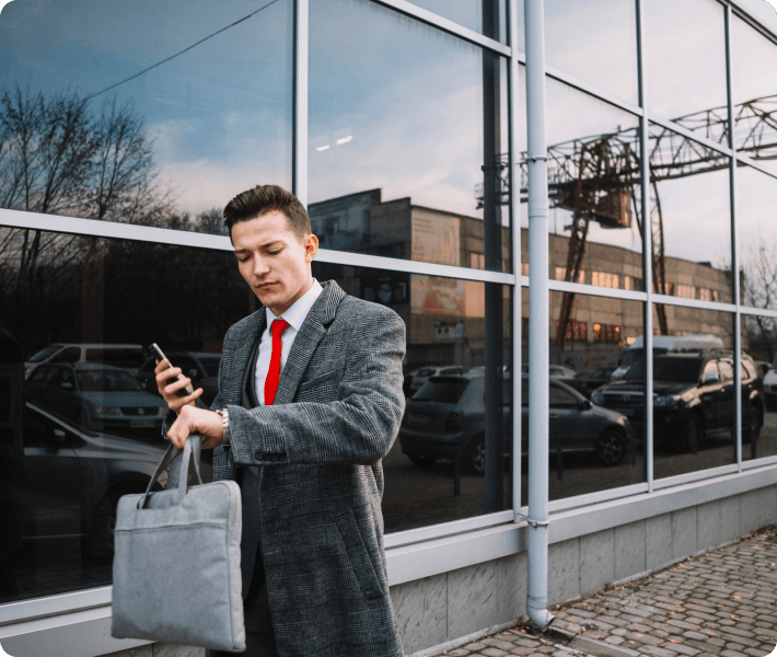 Dressed in a suit, a man holds a bag and gazes at his phone, reflecting a contemporary business environment.