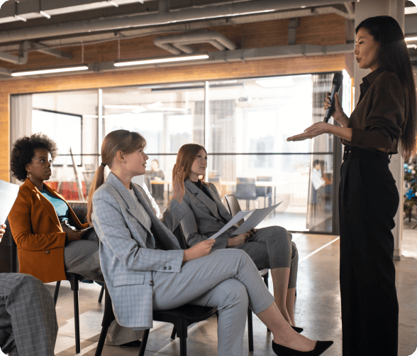 A woman delivers a presentation to an engaged audience of business individuals in a professional setting.